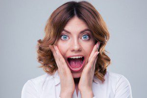 Scared face of woman over gray background. Looking at camera