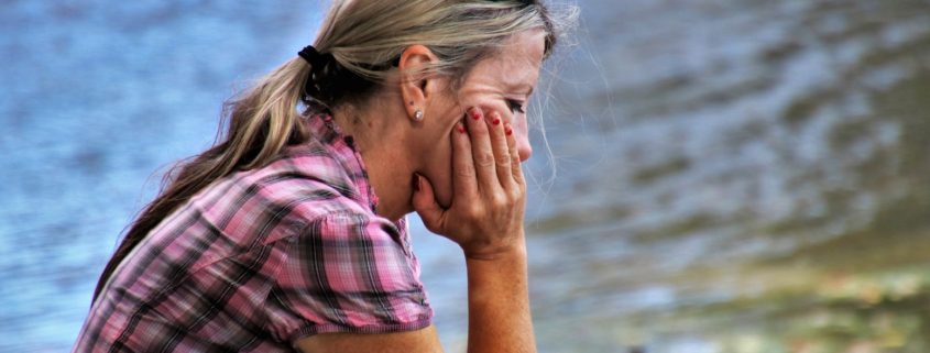 Frau mit Handy sitzt traurig am See