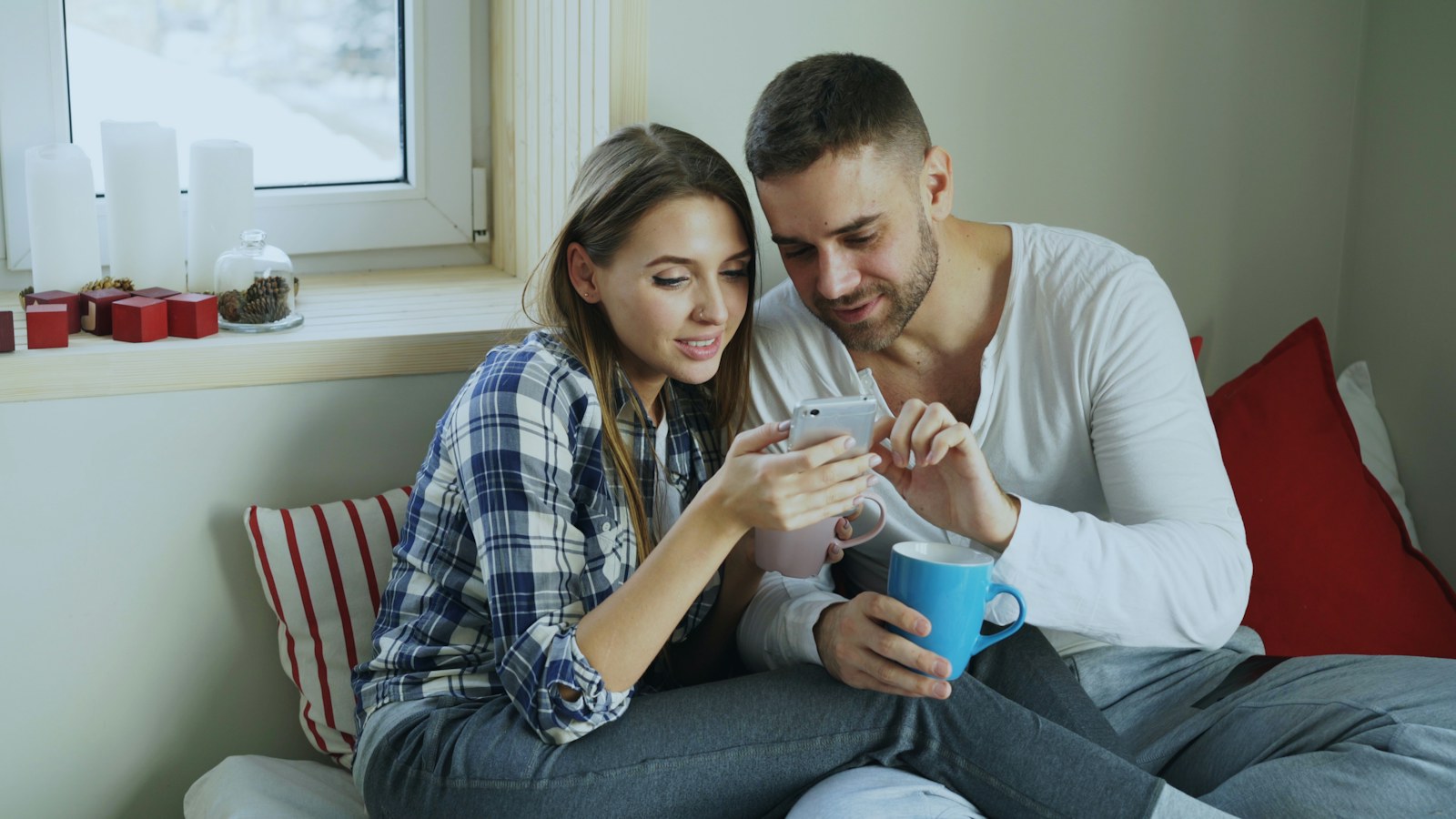 Ein Paar sitzt gemeinsam auf einem Bett und betrachtet ein Smartphone